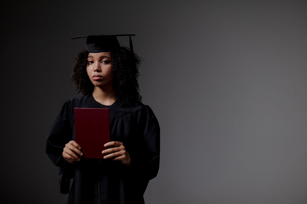 Young graduate in black academic regalia holds diploma, looking serious.